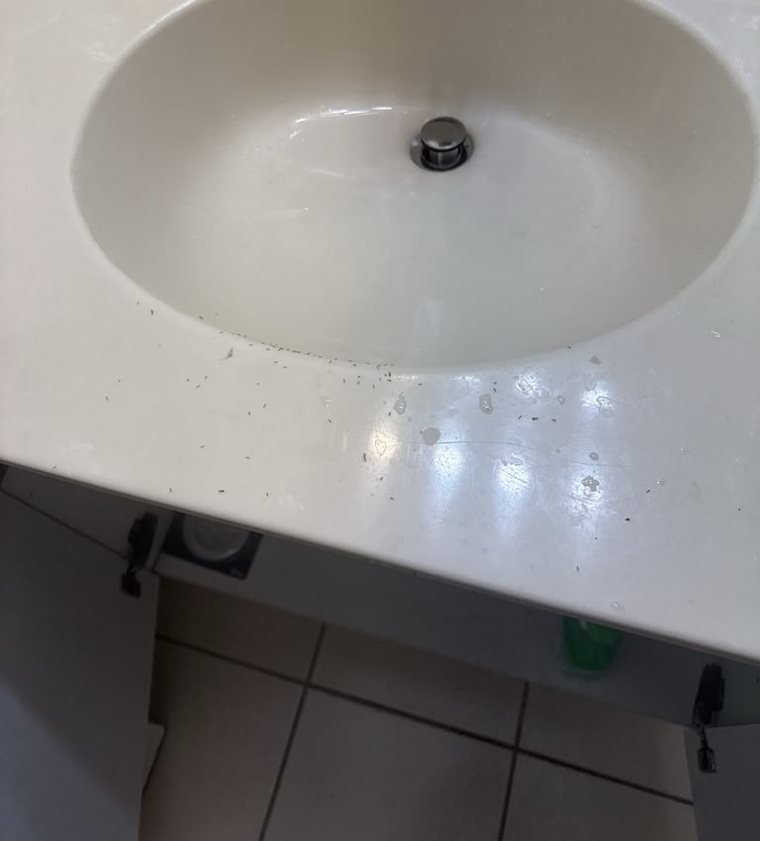 A cream bathroom vanity counter scattered with dust and small debris before cleaning, with the cabinet doors below removed