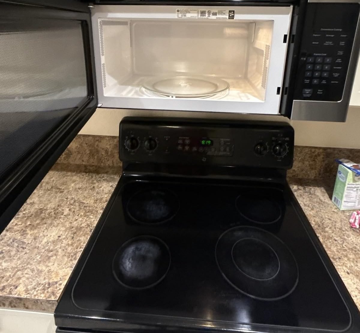 Cleaned black glass-top stove with the over-range microwave door open showing a wiped interior and clean turntable